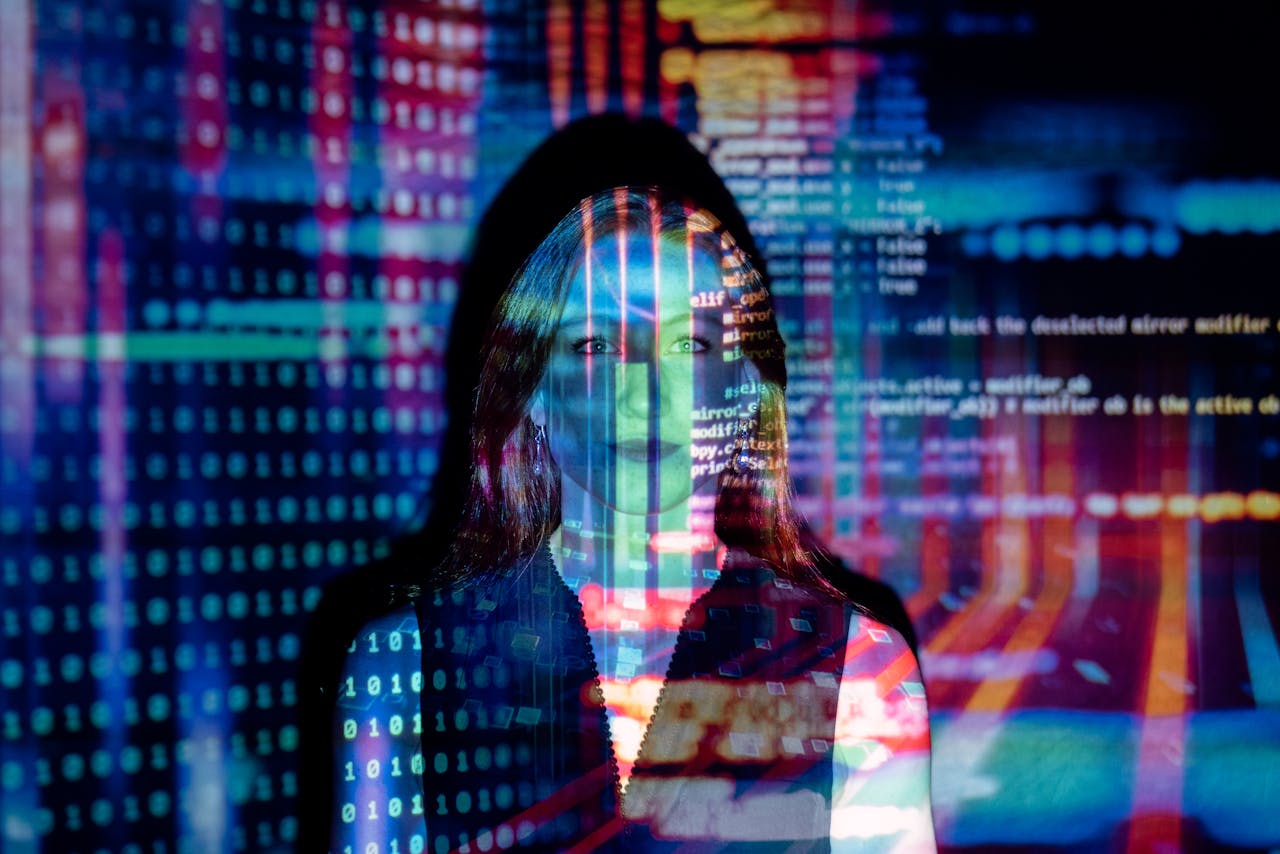 Woman staring straight ahead in dark room, with large screens of computer code projected over her