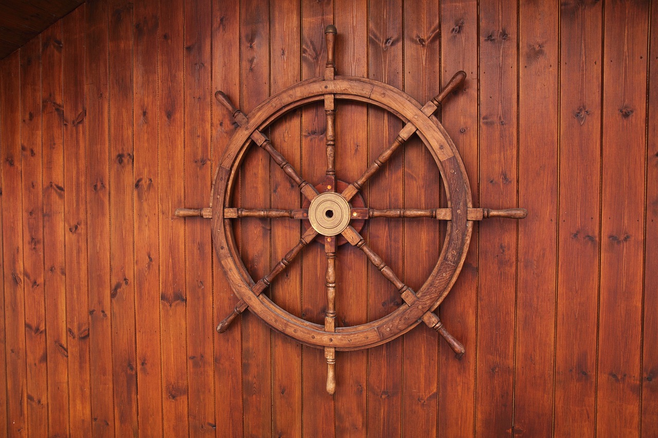 Wooden ships wheel, mounted on wooden wall.